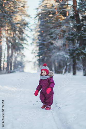 little cute girl 2 years old in lilac overalls walks in a winter snowy forest