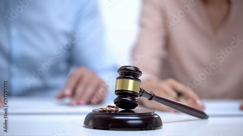 Marriage rings and gavel closeup, spouses signing divorce document on background