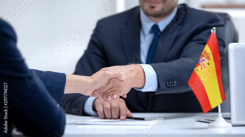 Spanish boss signing employment contract with immigrant employee, shaking hand