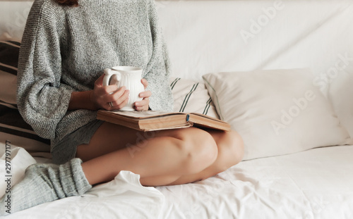 girl in home clothes on the couch reads a book and drinks a hot drink photo