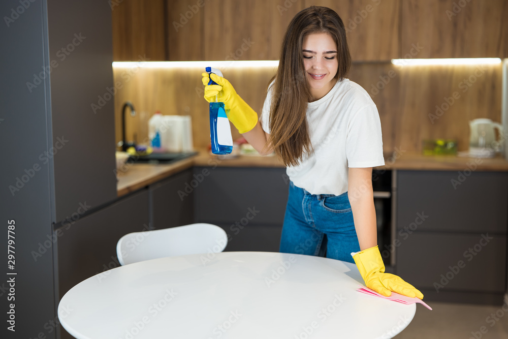 young beautiful woman in yellow gloves with detergent spray in her hand doing cleaning wiping dust off from the kitchen table with a rag young beautiful woman in yellow gloves with detergent spray in her hand doing cleaning wiping dust off from the kitchen table with a rag