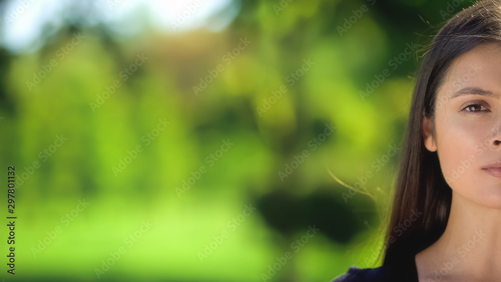Obraz premium Half-face of young woman looking camera on blurred green background, template