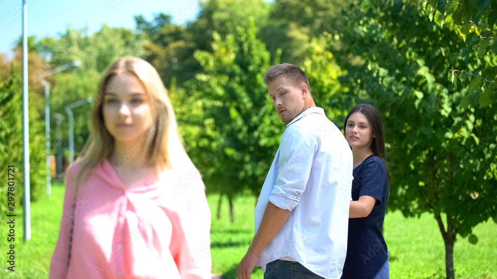 Man looking passing blond woman walking park with girlfriend, relations conflict Man looking passing blond woman walking park with girlfriend, relations conflict
