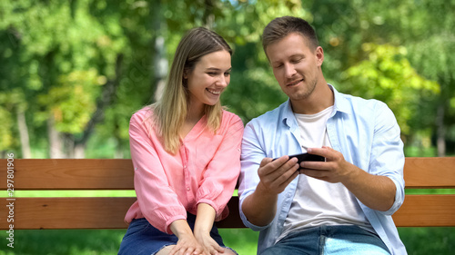 Young smiling woman and man watching online video by smartphone app on date