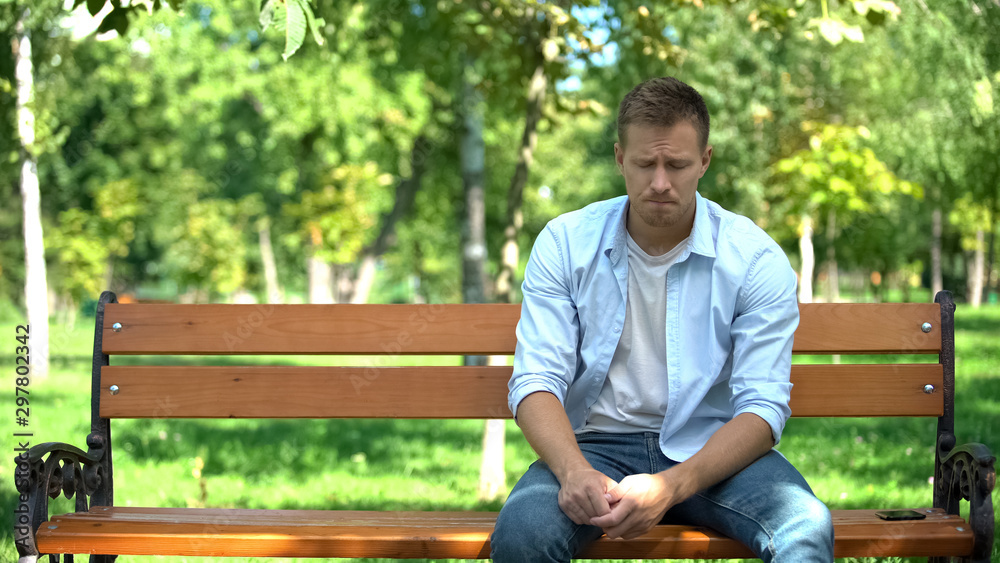 Sad young man sitting alone park bench, breakup crisis, problem hopelessness Sad young man sitting alone park bench, breakup crisis, problem hopelessness