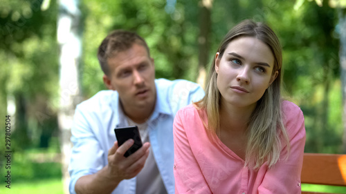 Annoyed girlfriend listening jealous boyfriend holding phone checking messages © motortion