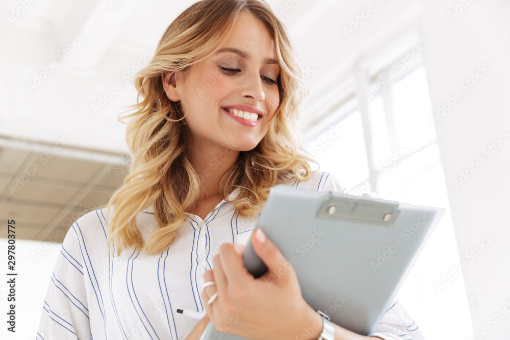 Image of joyful secretary woman smiling and holding clipboard in office Image of joyful secretary woman smiling and holding clipboard in office