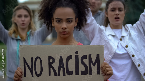 Afroamerican girl holding No racism sign, activists chanting Human rights slogan © motortion