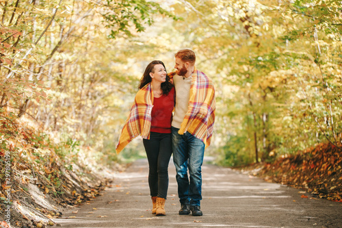 Beautiful couple man woman in love. Smiling laughing boyfriend and girlfriend wrapped in yellow blanket walking in park on autumn fall day. Togetherness and happiness. Authentic real people. © anoushkatoronto