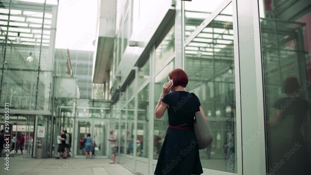 Rear view of young woman commuter with smartphone and coffee walking outdoors in city. Rear view of young woman commuter with smartphone and coffee walking outdoors in city.
