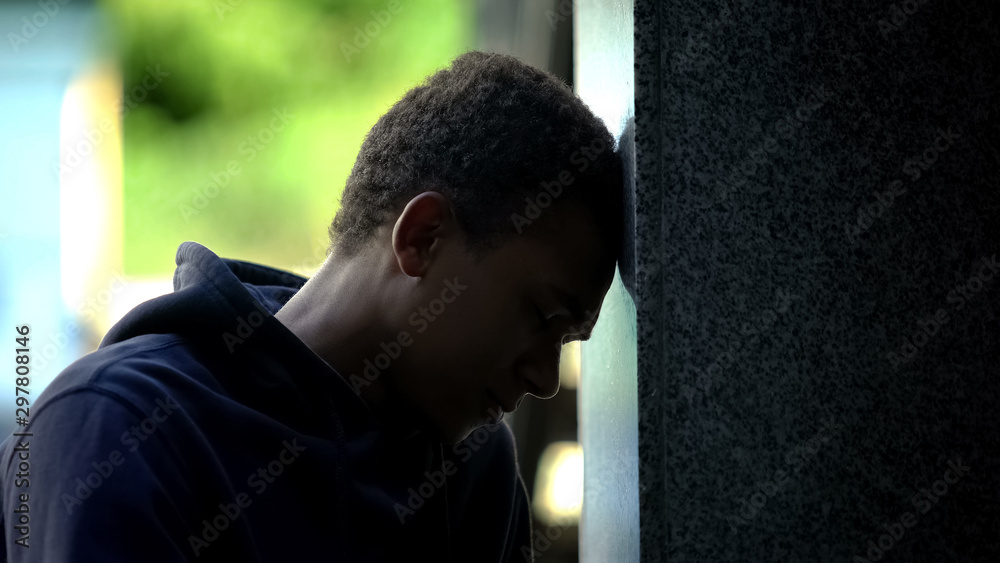 Obraz premium Depressed african american teenager sitting outdoor leaning on wall, crisis