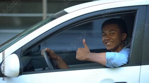 Mixed-race teenager sitting on driver seat of car showing thumbs-up, driving