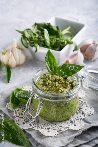 traditional italian basil pesto sauce in a glass jar on a light stone table Vertical