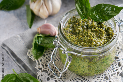 traditional italian basil pesto sauce in a glass jar on a light stone table Close up