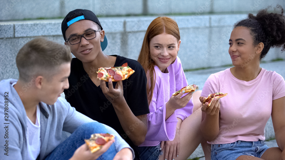 Joyful young people enjoying time together eating pizza outdoors, friendship