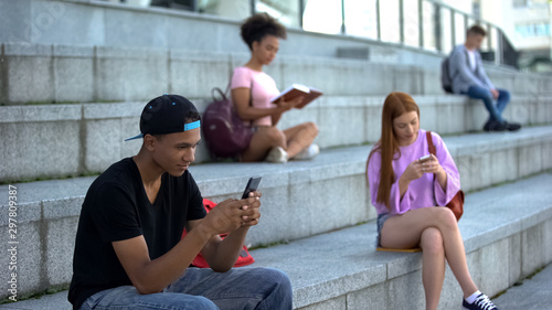Black male teenager chatting smartphone outdoors, high school students on break