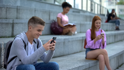 Happy male student playing smartphone game outdoors, gadget addiction, chat