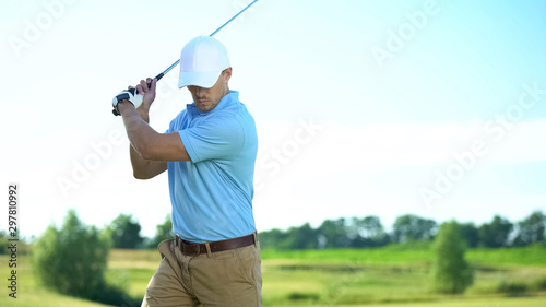 Handsome golfer ready to hit ball, taking swing position, club-and-ball sport