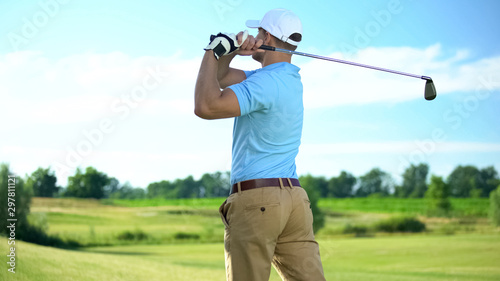 Experienced golf player hitting ball in draw position at course, back view