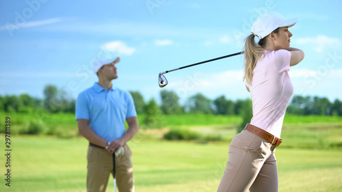 Female golfer hitting ball at course, male coach watching successful shot, sport