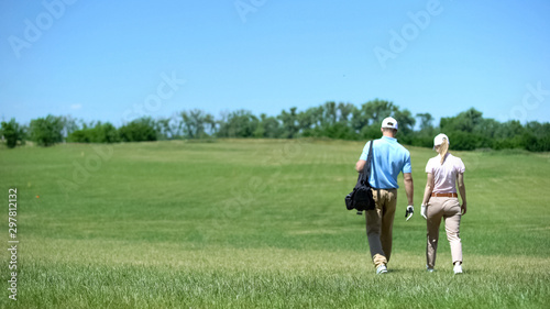 Couple of male and female golfers walking on course with clubs bag, lesson © motortion