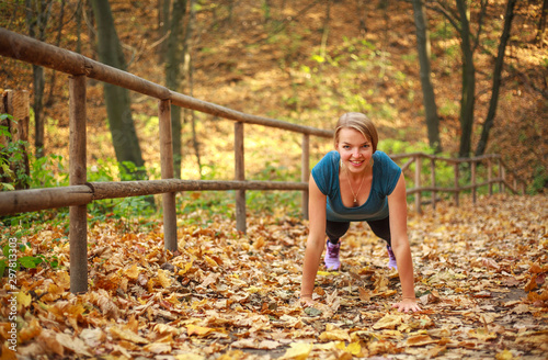 Young slim woman doing fitness exercise stretching in autumn forest park, sport and healthy lifestyle