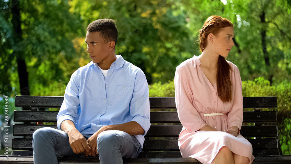 Offended teenagers sitting on bench turned from each other, misunderstanding