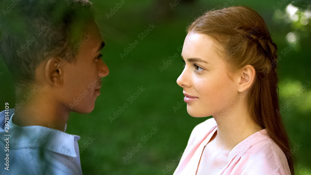 Multi-ethnic teenage couple looking at each other in park, trustful relations Multi-ethnic teenage couple looking at each other in park, trustful relations