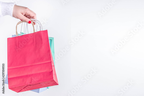 Christmas shopping and sale concept. Buying Christmas gifts. Woman hand hold pastel colored paper bags with xmas and New Year gifts. On white background copy space