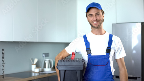 Handyman holding tools standing in kitchen, professional plumbing services