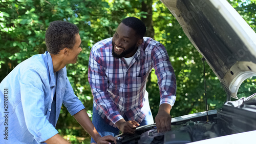 Black father explaining car structure to son and smiling, teamwork, family