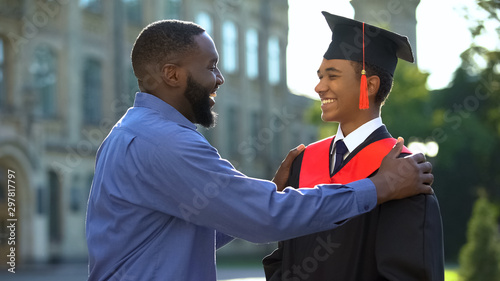 Afro-american father feeling glad graduating son university mantle, achievement