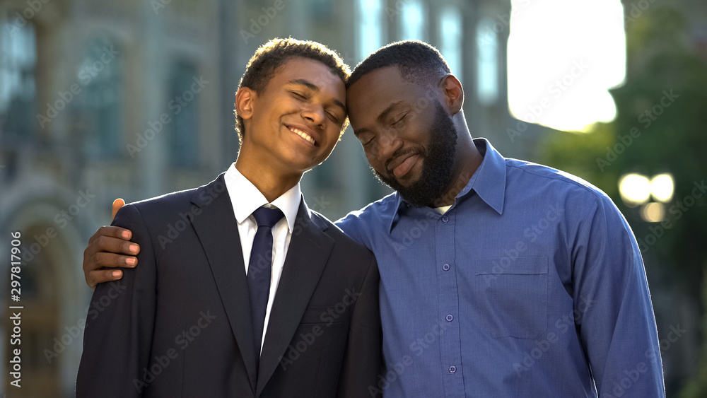 Male teenager in suit and happy father smiling, celebrating prom near university