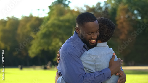 Caring afro-american dad embracing teen son in park, family relationships, love