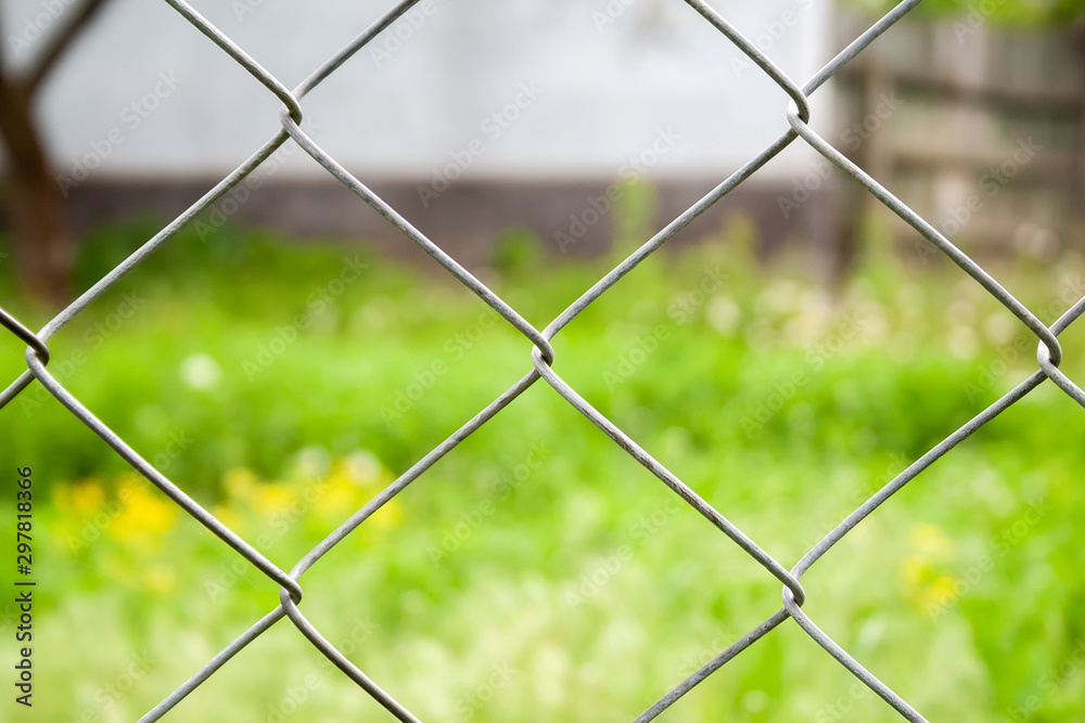 Blurred countryside view through a metal fence on green grass and a house Blurred countryside view through a metal fence on green grass and a house