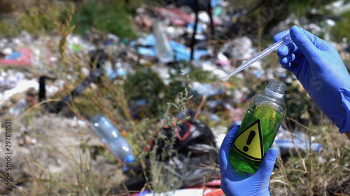 Ecologist taking sample from bottle with warning sign against waste background