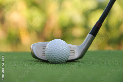 Golf club and golf ball close up in grass field with sunset.