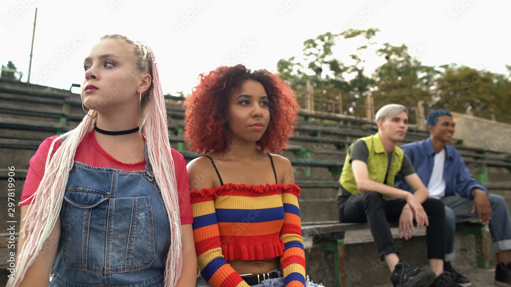 Obraz premium Stylish teenage girls sitting on stadium bench apart from boys, feeling shy