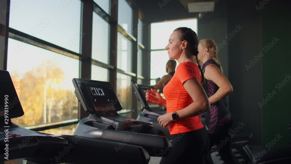 Cute young girl running on a treadmill in front of panoramic Windows in the fitness room. Gym with treadmill and large Windows