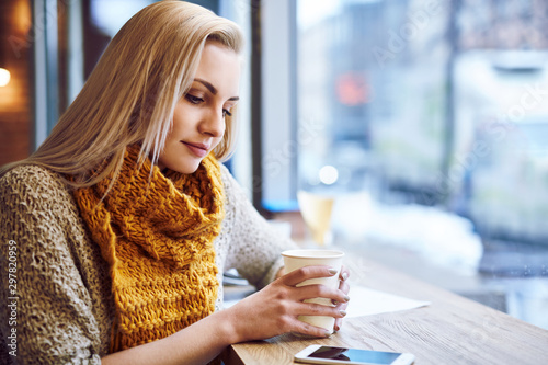 Beautiful young woman warming up in cafe during cold winter day.