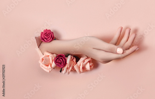 Hand with paper flowers and painted nails is thrust through a hole in the paper background. Cosmetics and hand care, moisturizing and wrinkle reduction