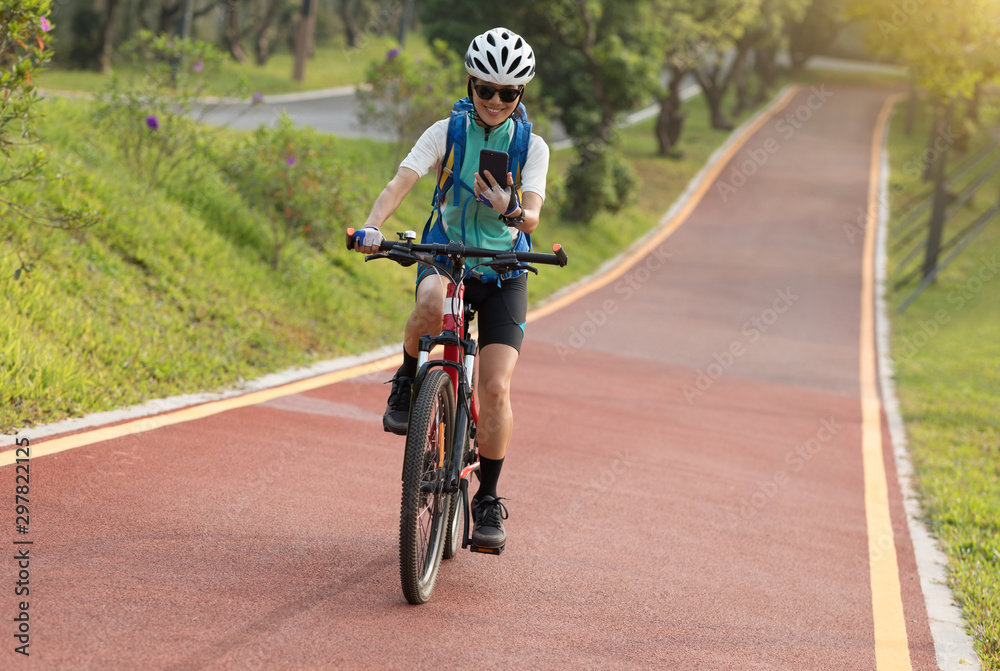 Riding on park bike path,using smartphone while riding bike on sunny day Riding on park bike path,using smartphone while riding bike on sunny day