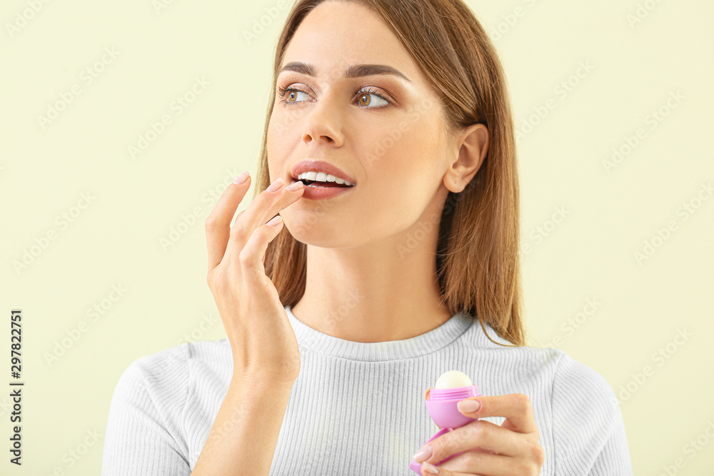 Beautiful young woman with lip balm on color background