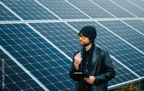 thinkihg man with clipboard, standing beside solar panels photo