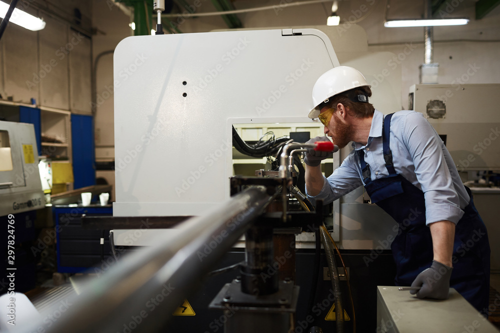 Young operator in protective glasses and workwear standing and working on lathe in the factory Young operator in protective glasses and workwear standing and working on lathe in the factory