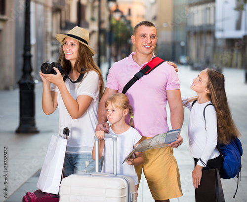 Positive tourist family of four using map and camera