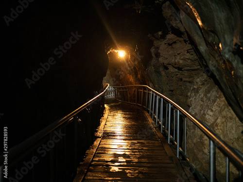 A wet wooden walkway bridge through a dark lit cave