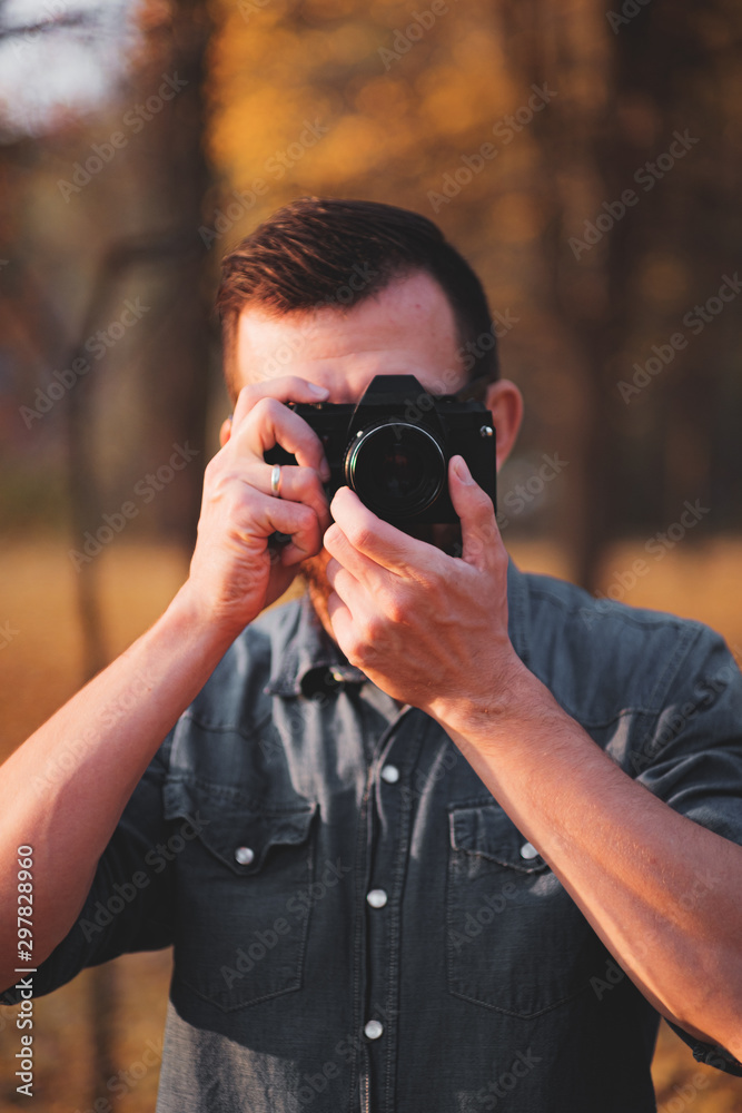Man taking a photo with a vintage camera. Portrait of a photographer in an autumn outdoor environment