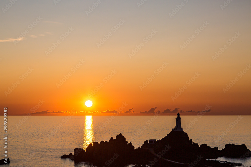 Sunset at Corbiere on the island of Jersey, with the rocks and lighthouse silhouetted against the dramatic sky