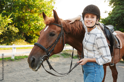 Image of beautiful woman wearing hat standing by horse at yard
